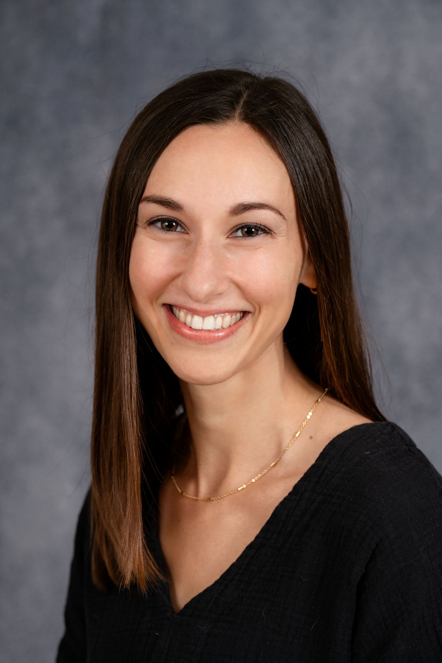 Professional portrait of person in black v-neck top with delicate necklace.