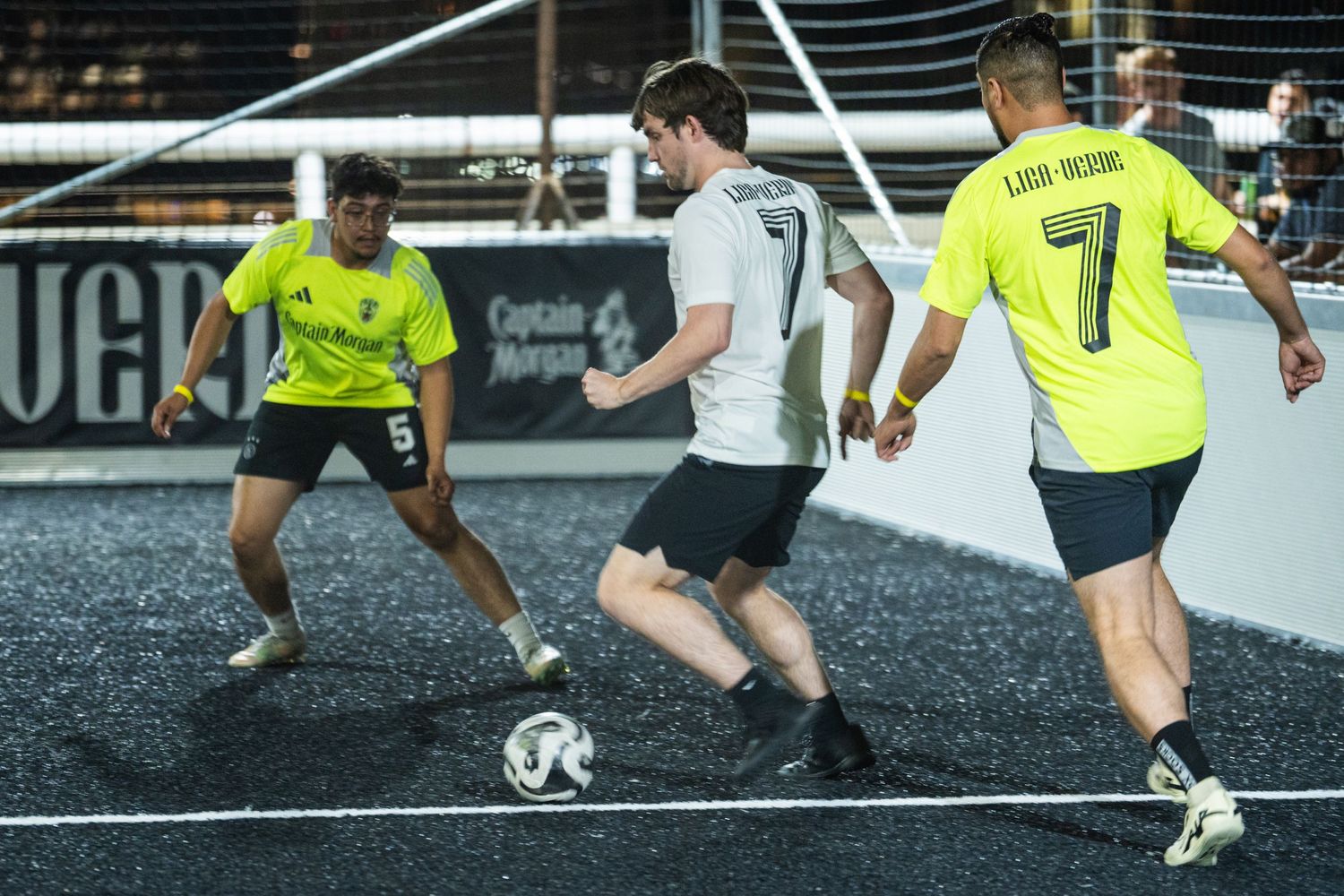 Soccer match in progress on artificial turf with players in yellow and white uniforms.