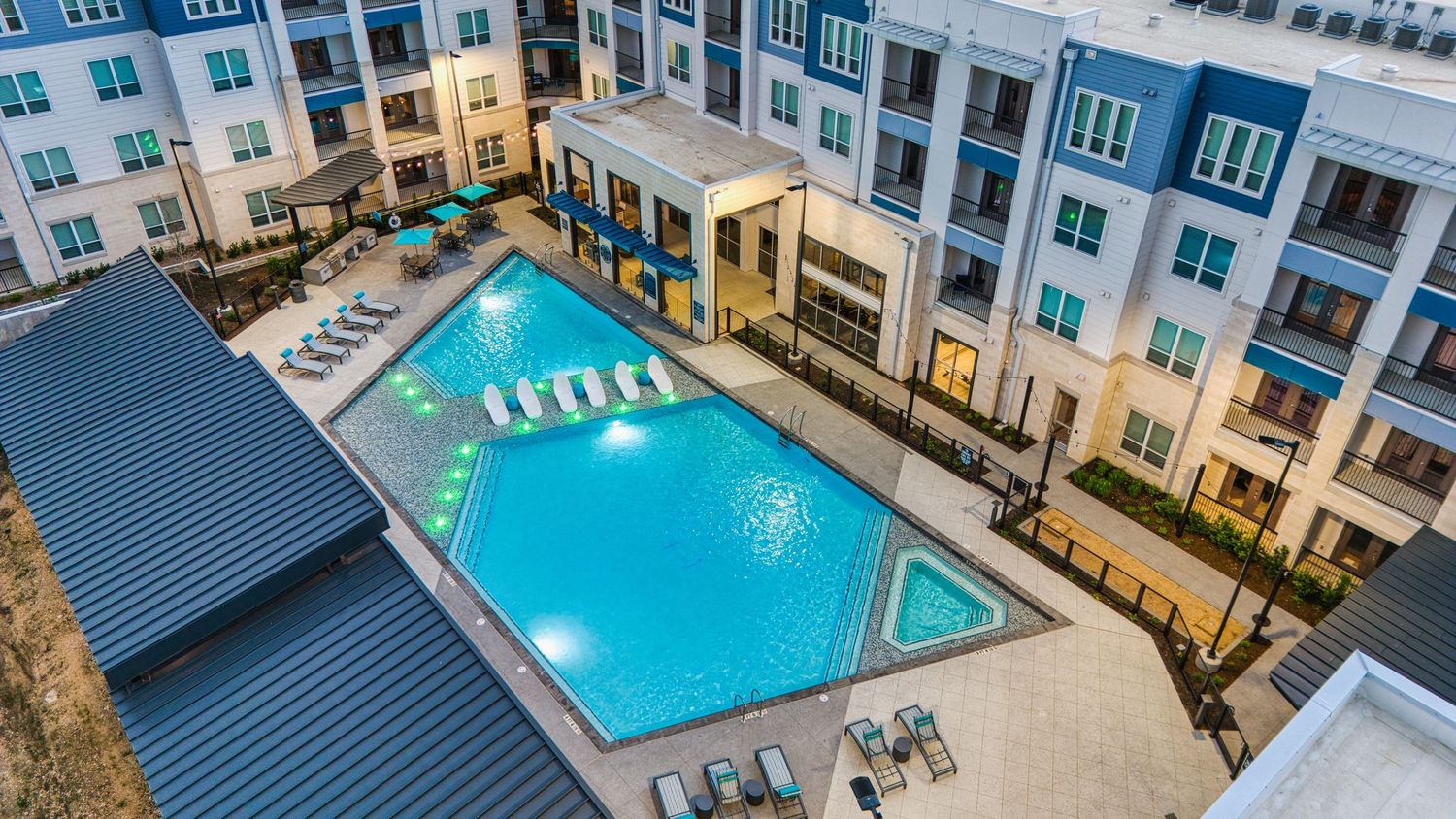 Luxury apartment community pool area with covered pavilion and blue accent lighting at twilight.