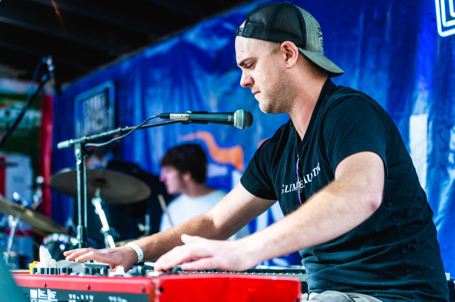 Musician plays keyboard on stage with blue lighting and microphone setup.