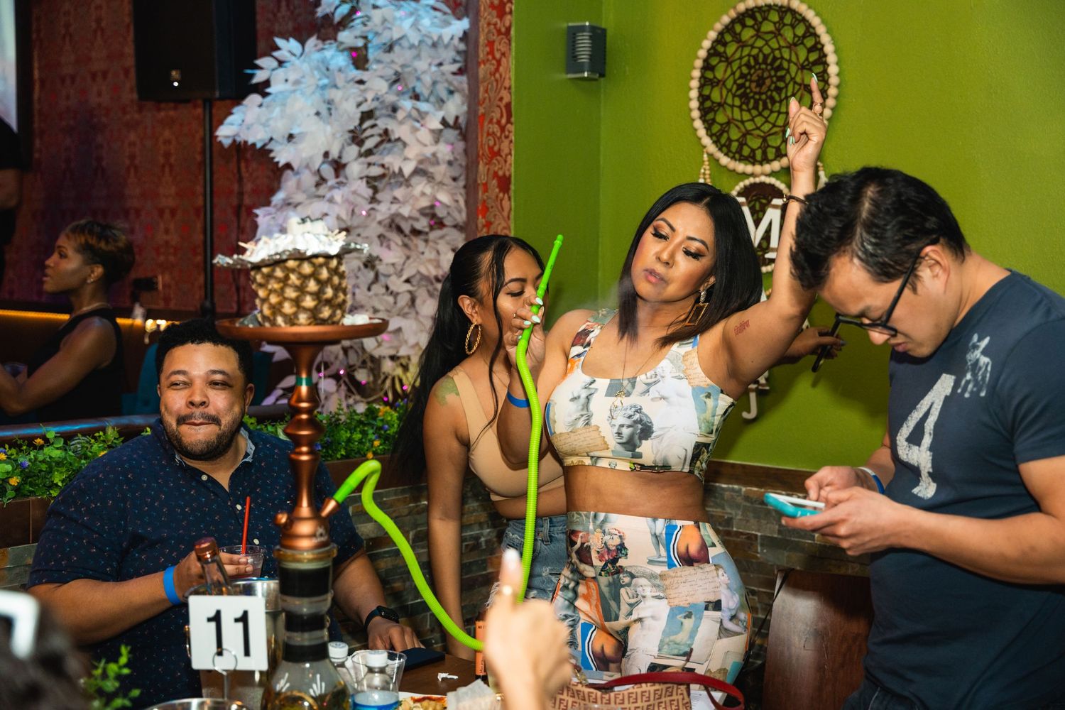 Group enjoying hookah and drinks at colorful restaurant table with festive atmosphere.