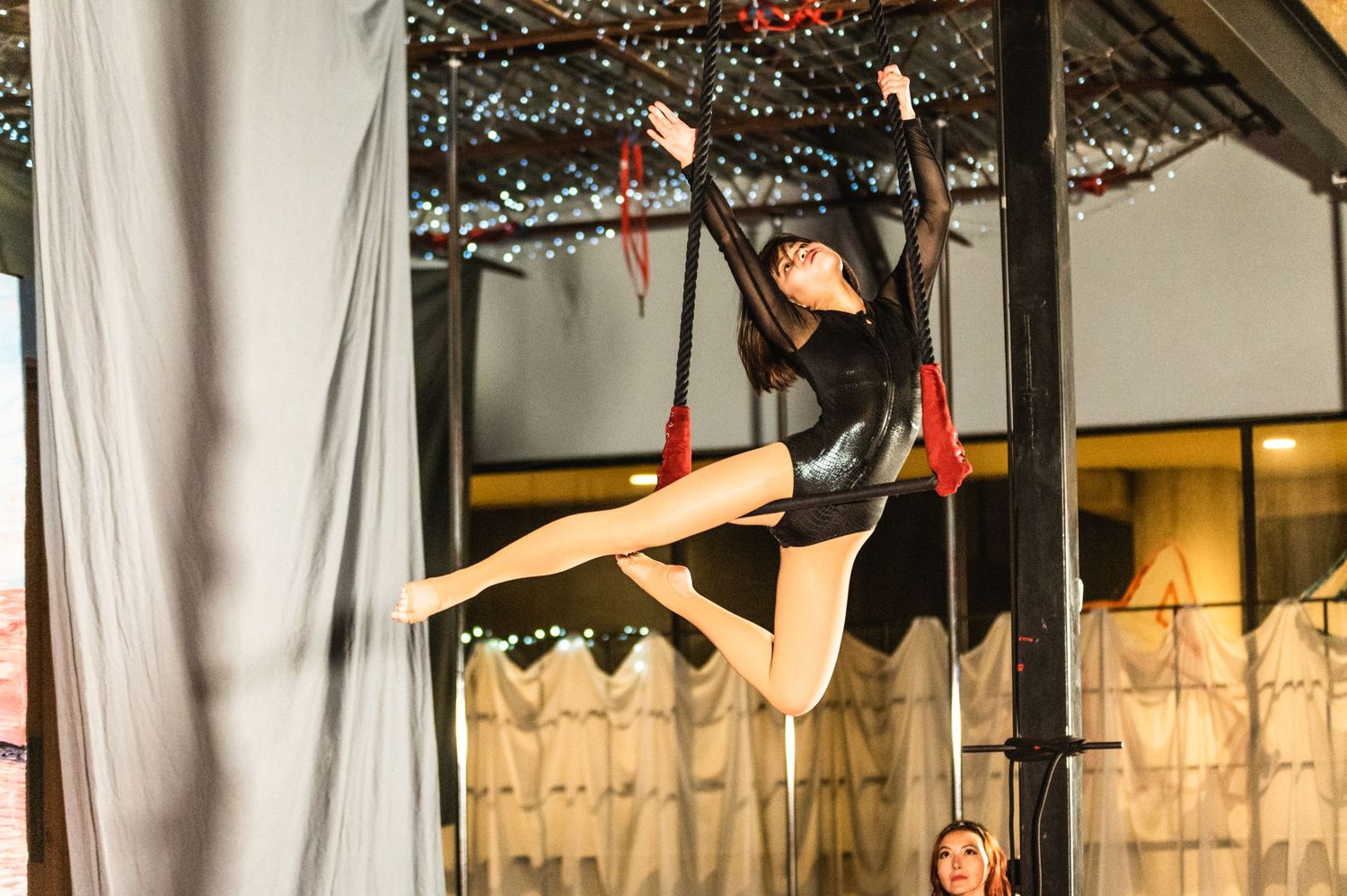 Dancer performing splits while suspended from aerial equipment in studio space.
