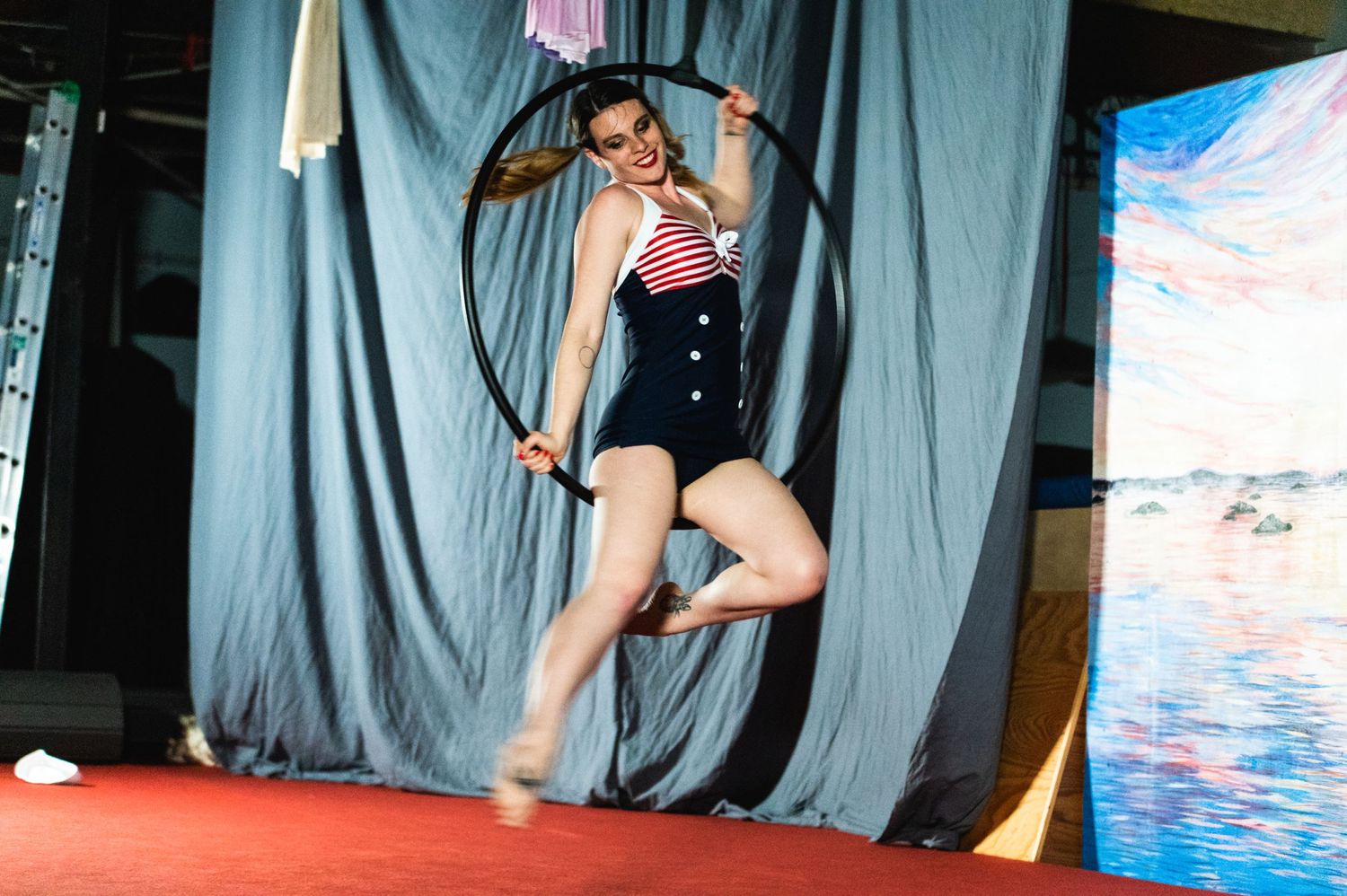 An aerial artist performs on a lyra hoop against a grey curtain backdrop.