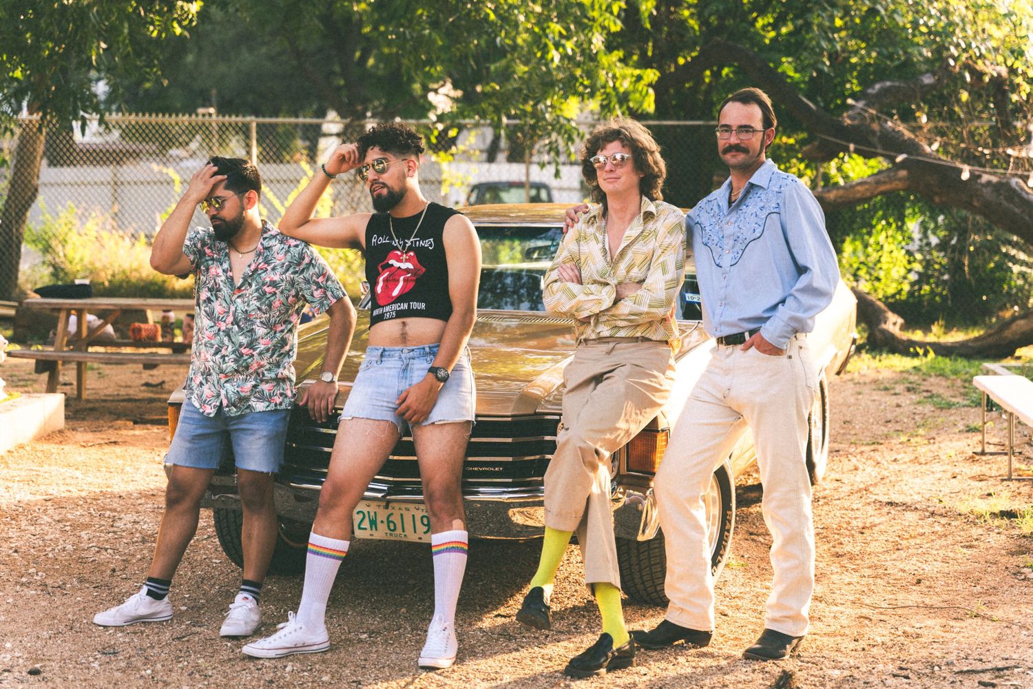 A group of friends sitting casually on the back of a truck in a sunny outdoor setting.