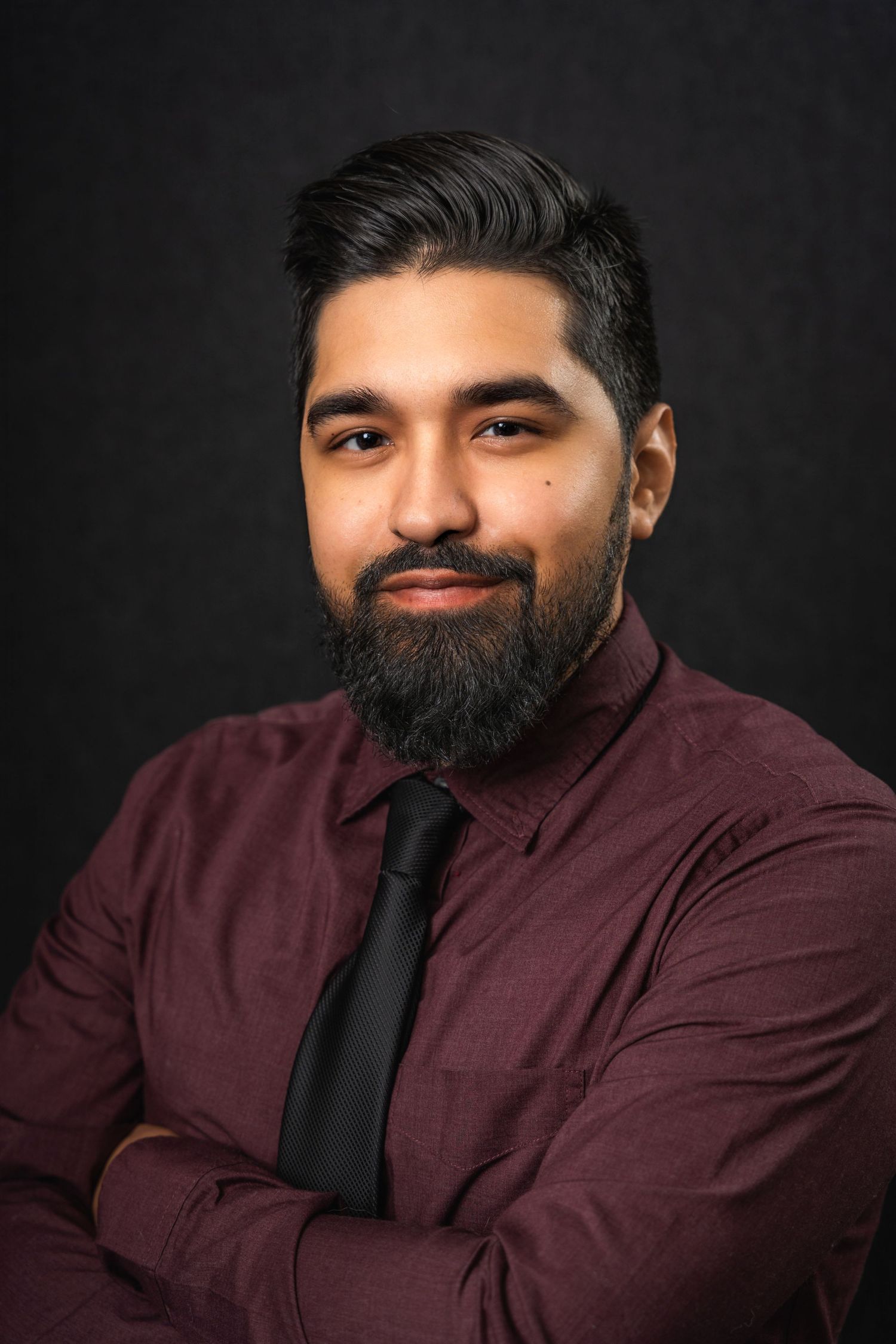 Professional portrait of person in burgundy shirt and black tie against dark background.