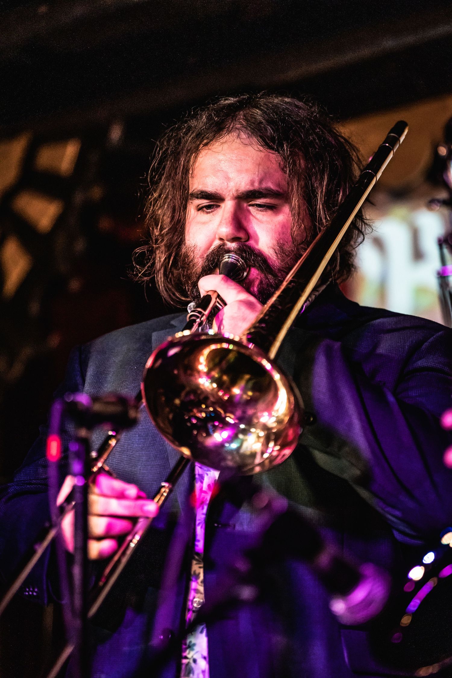 Passionate musician playing trombone during energetic live performance in purple stage lighting.