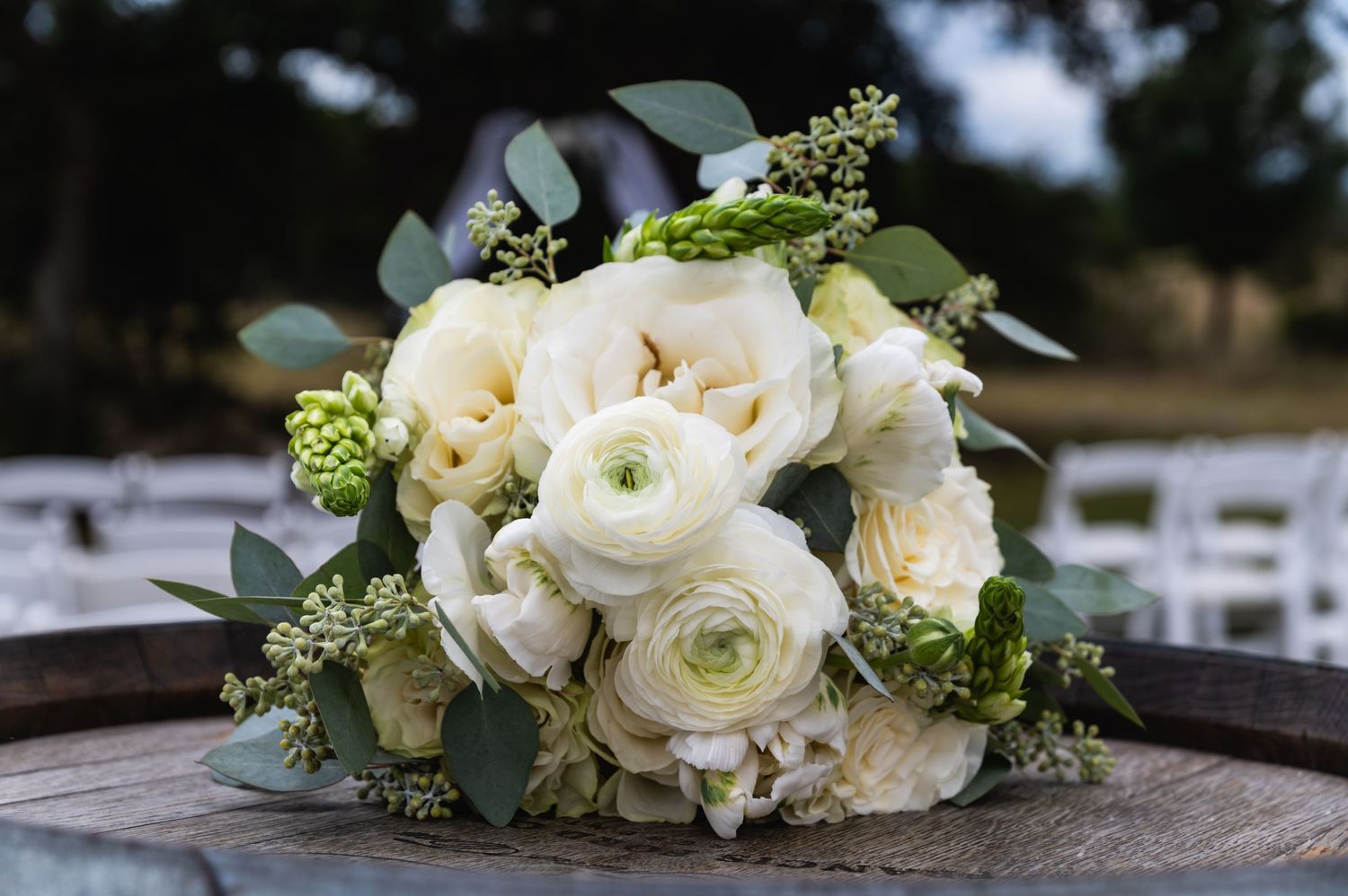 Elegant white and cream wedding bouquet with roses, ranunculus, and eucalyptus leaves.