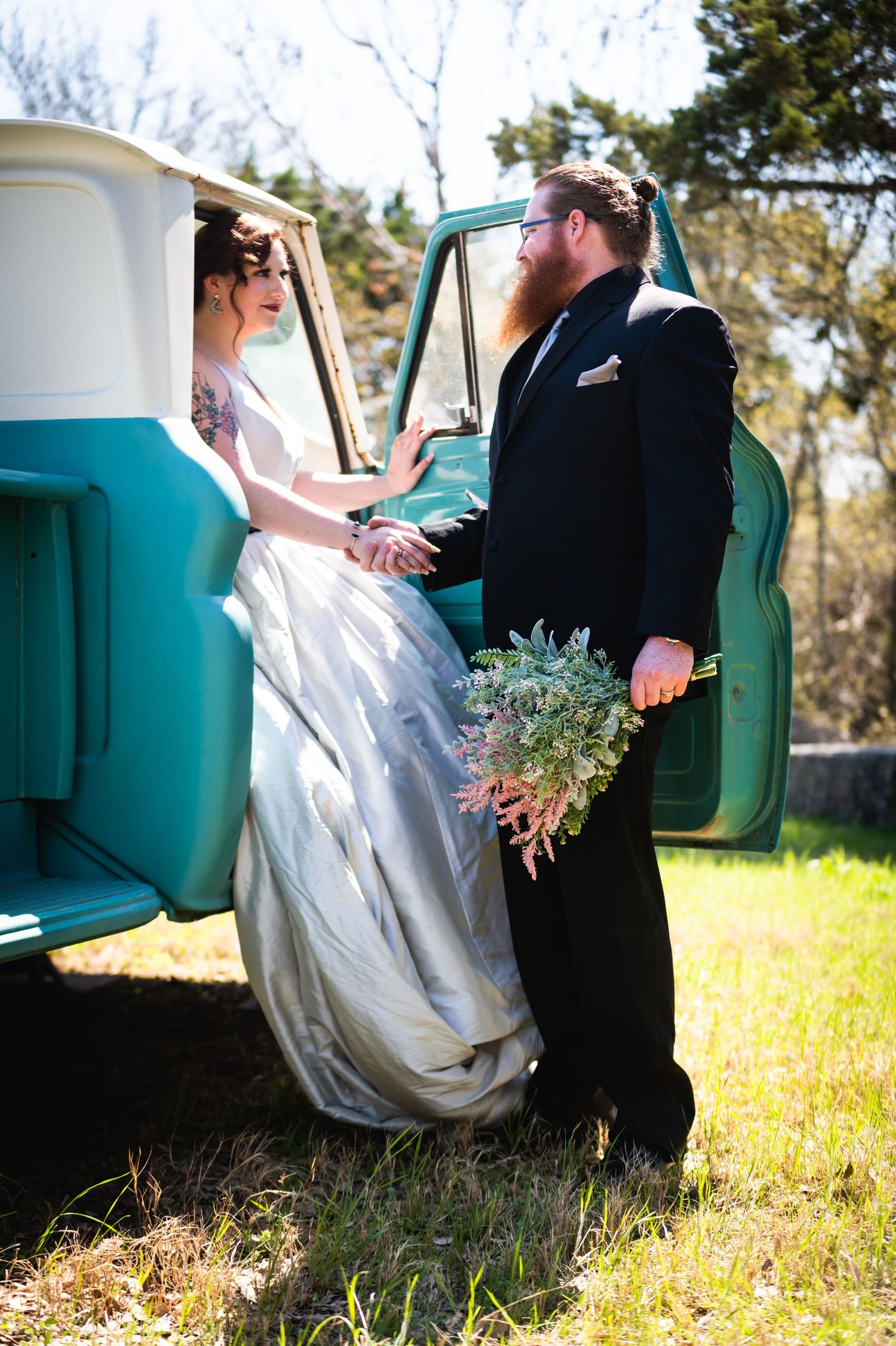 A romantic moment shared between newlyweds by a vintage turquoise truck in a sunny field.