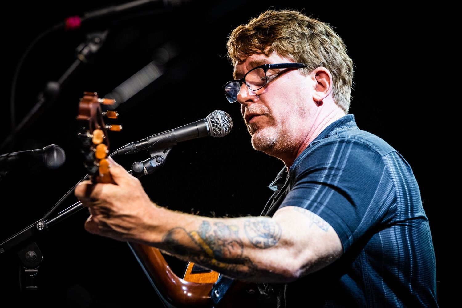 Energetic musician performs on stage with acoustic guitar under stage lighting.
