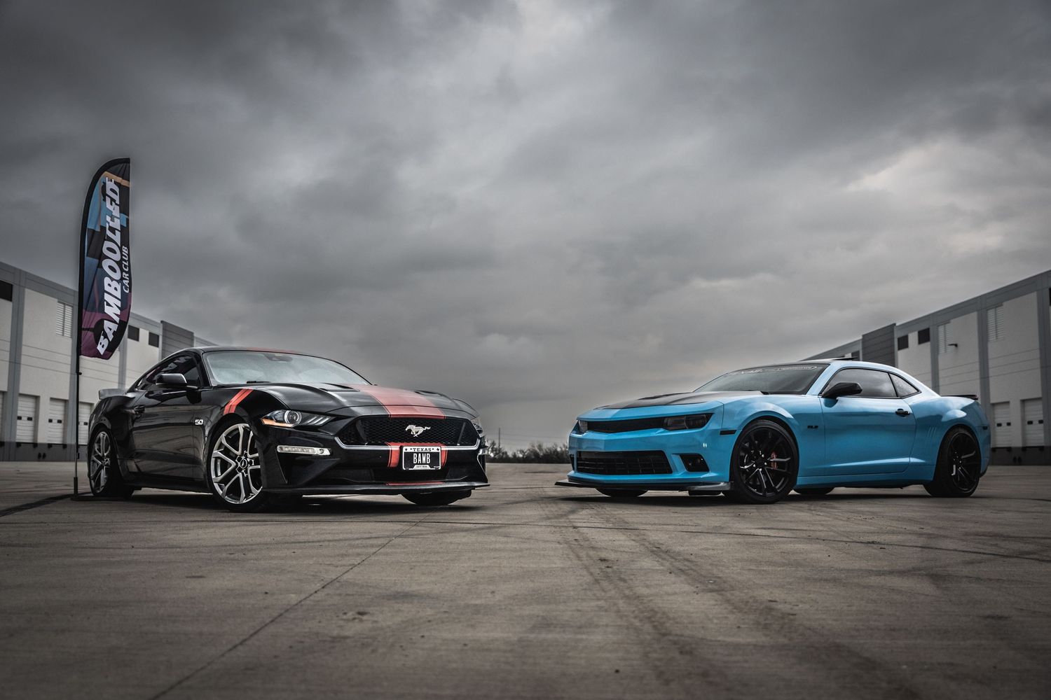 Black and blue sports cars parked side by side under dramatic stormy skies.