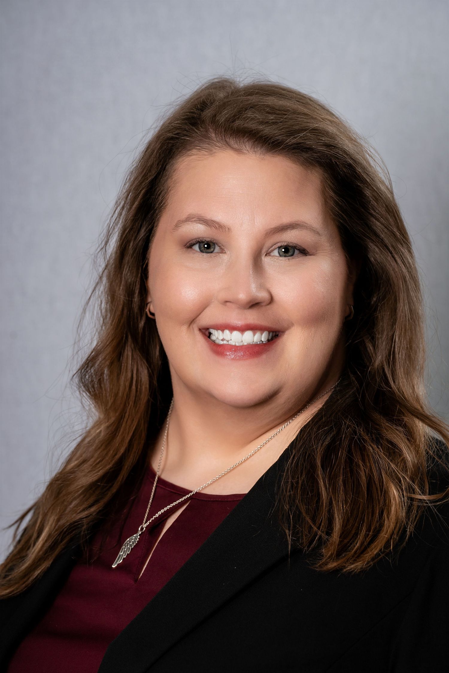 Corporate portrait of person wearing black jacket and burgundy top with necklace.
