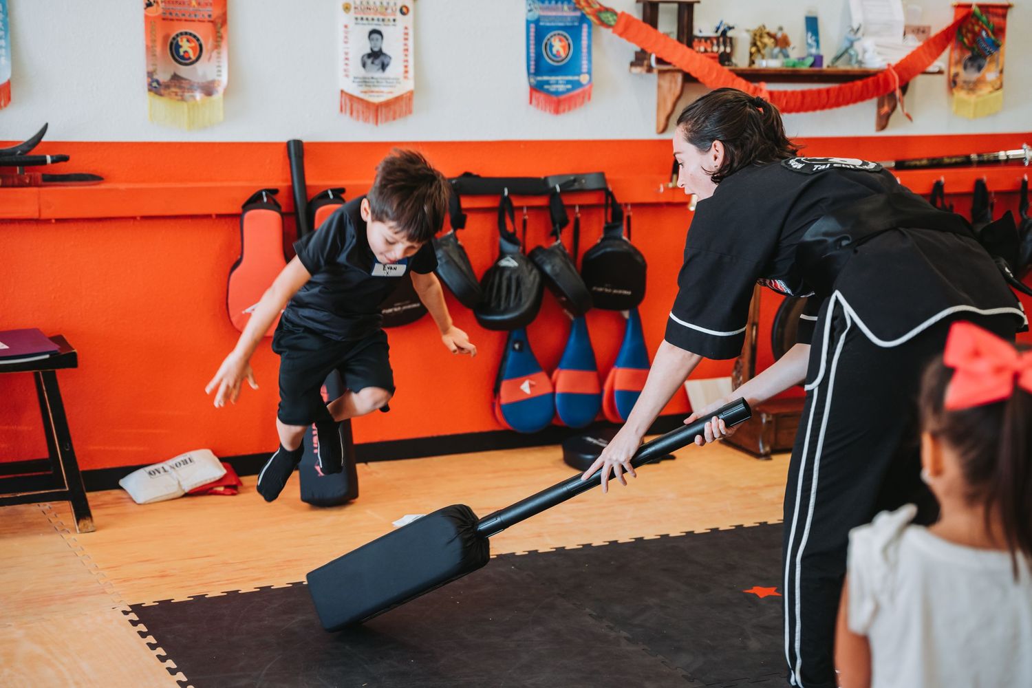 Students practicing with training equipment in a martial arts studio with orange and white walls.
