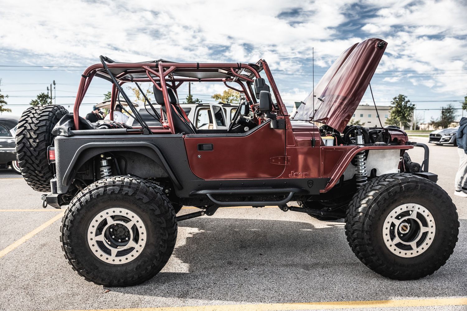 Side view of a heavily modified red Jeep Wrangler with exposed engine and massive off-road wheels.