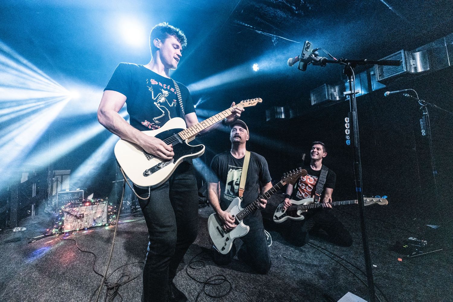 Rock band performing on stage with dramatic blue lighting and musicians playing guitars.