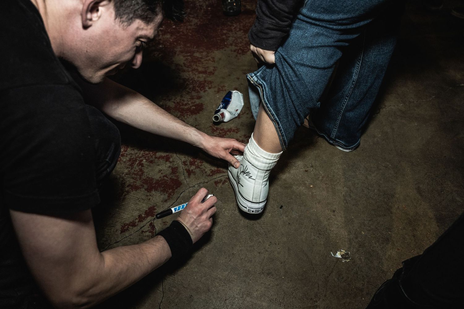 Concert attendee signing or marking white sneakers in dark venue setting.
