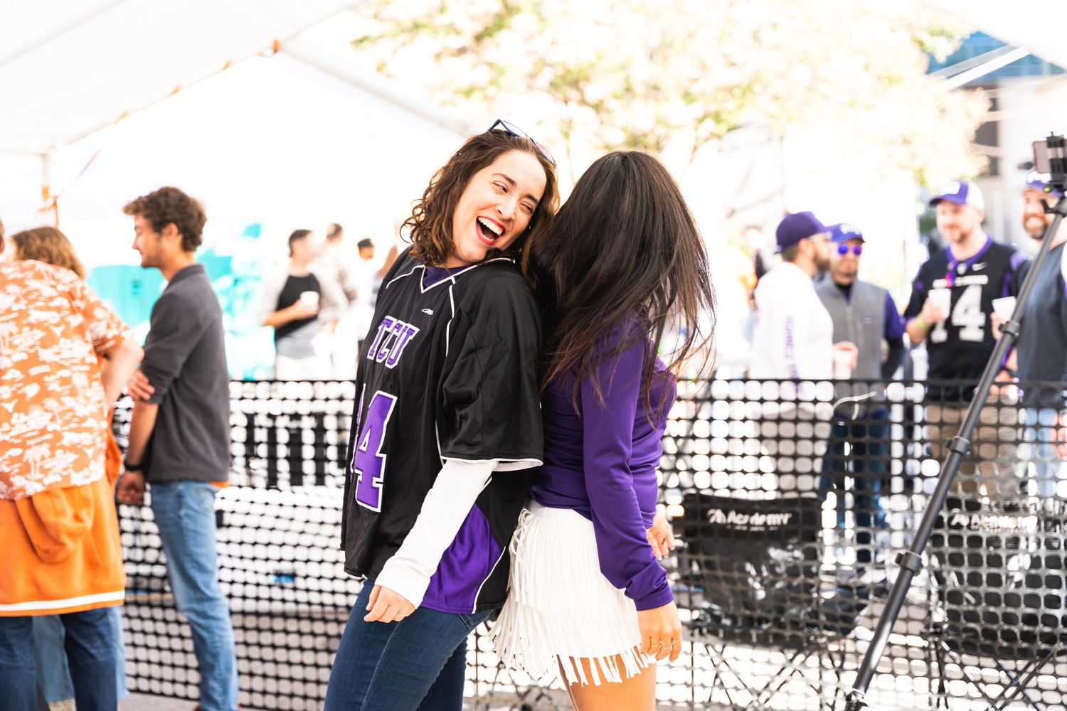 Two friends laughing and dancing together at an outdoor festival with crowd in background.