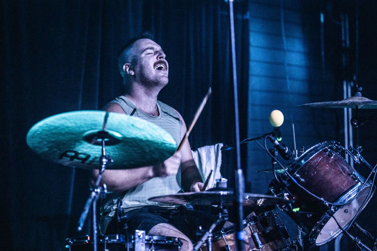 Drummer performs with enthusiasm under blue stage lighting.