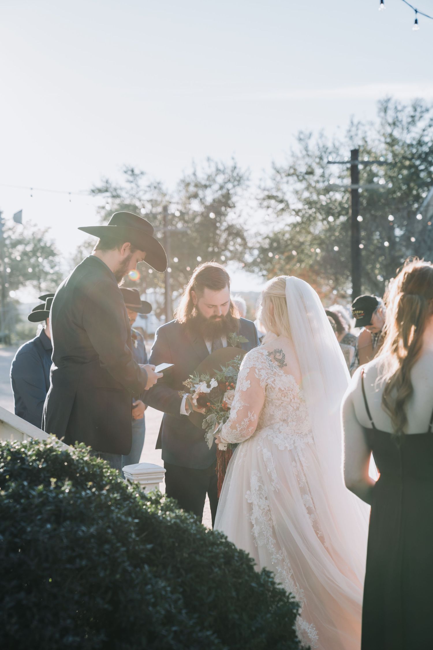 A wedding ceremony taking place outdoors with string lights and greenery in the background.