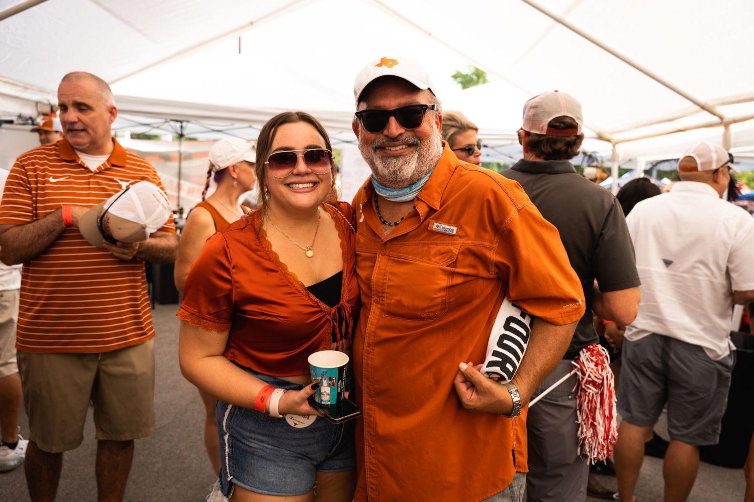 Fans wearing burnt orange University of Texas gear pose with drinks at a tailgate party.