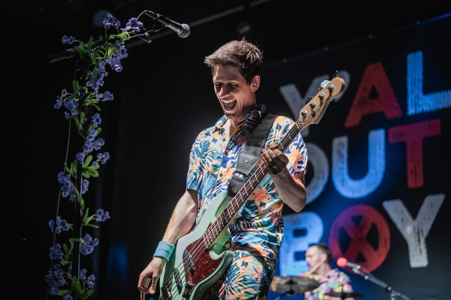 Musician plays electric guitar on stage with colorful neon lights and floral decorations in the background.