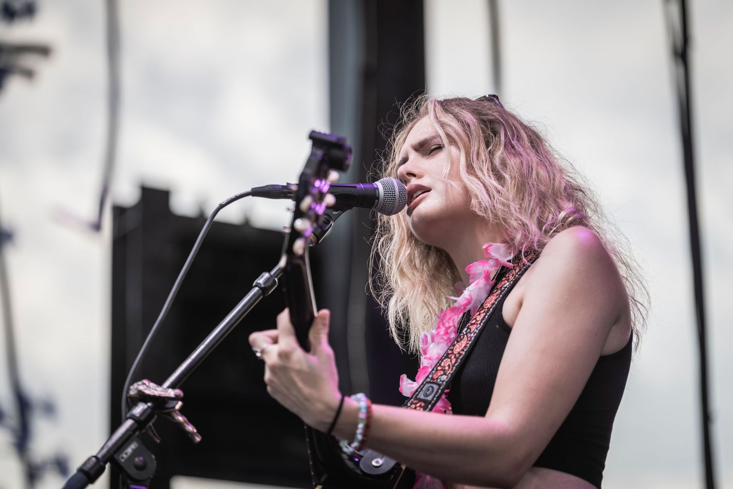 Musicians perform on stage with instruments and pink decorative elements at an outdoor concert venue.