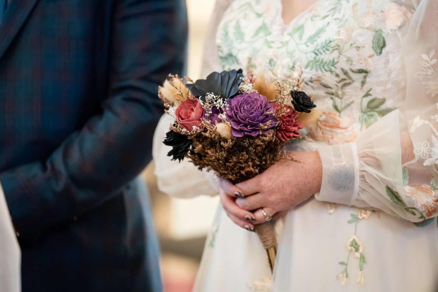A close-up of a wedding bouquet with purple, orange and burgundy flowers held against a floral dress.