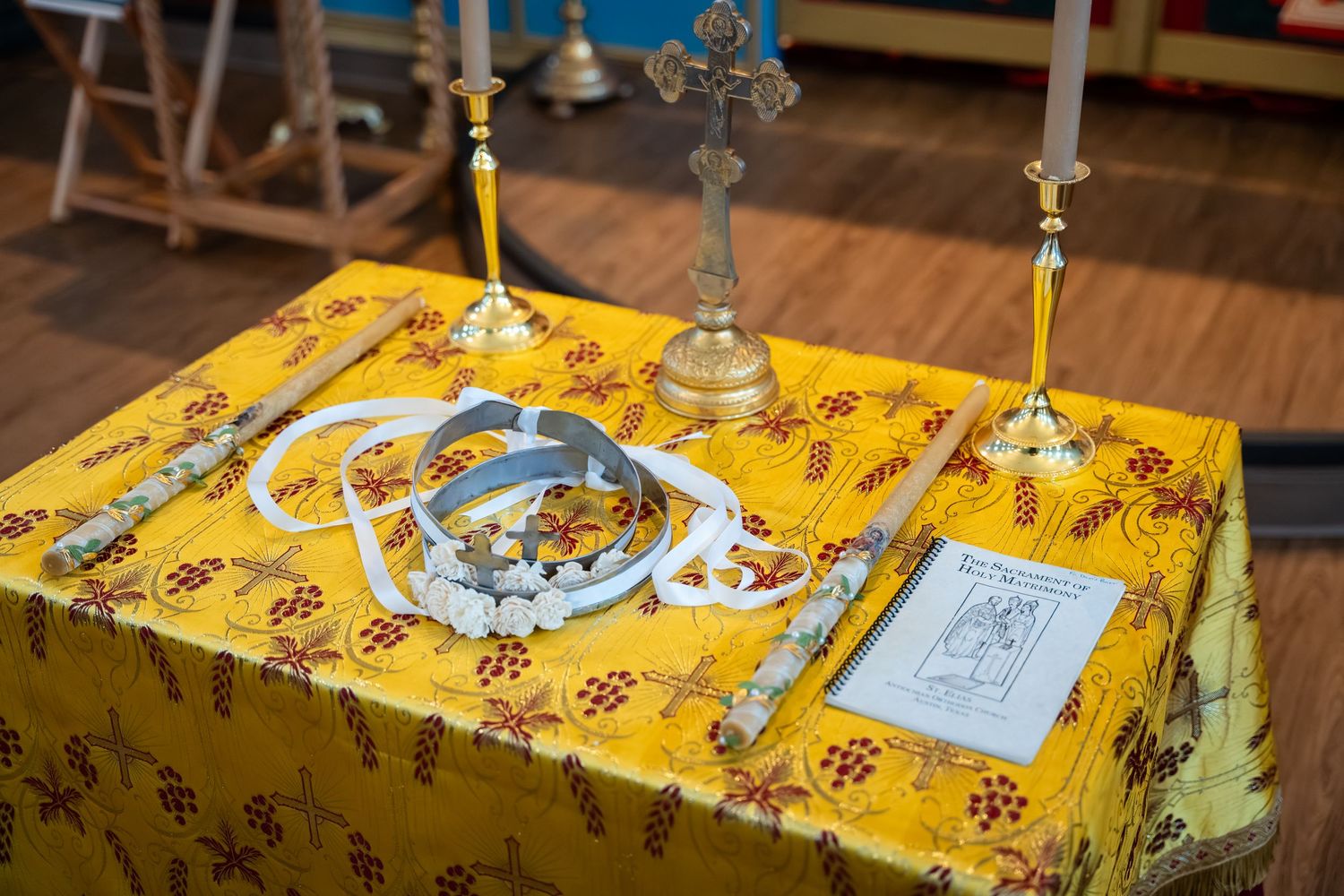 Orthodox Christian altar setup with cross, candlesticks and liturgical items on a yellow floral tablecloth.