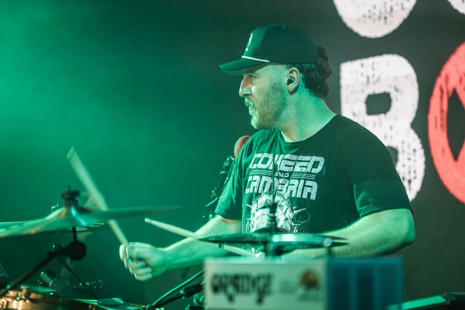 DJ performs at a nightclub with green lighting and electronic equipment visible in the background.