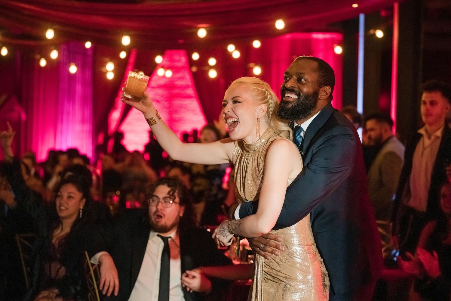 People dancing and celebrating at a wedding reception with pink lighting and glowing orb lights in the background.