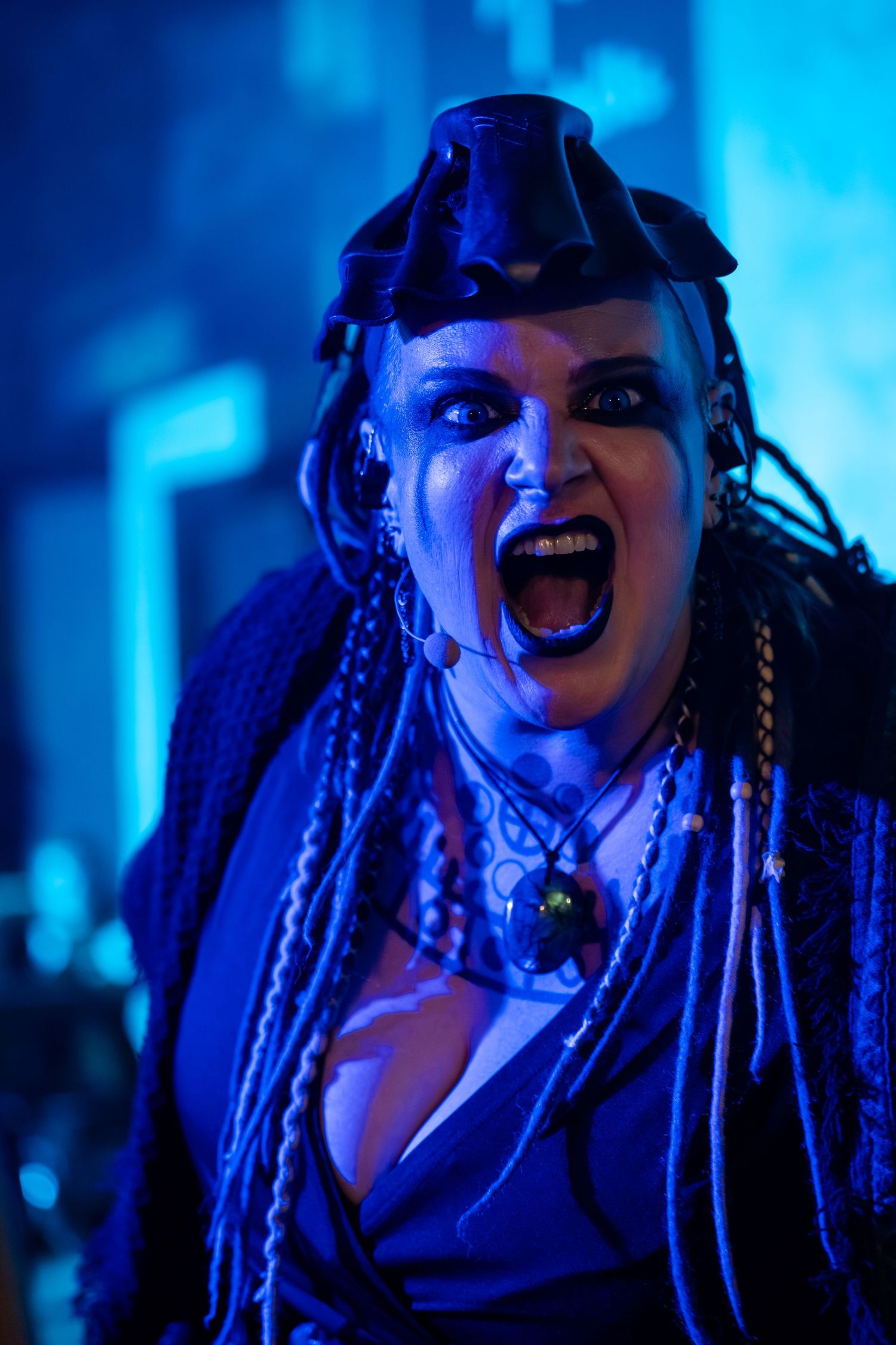 A performer with dark braids and dramatic makeup poses expressively against a blue-lit background in a sequence of shots.
