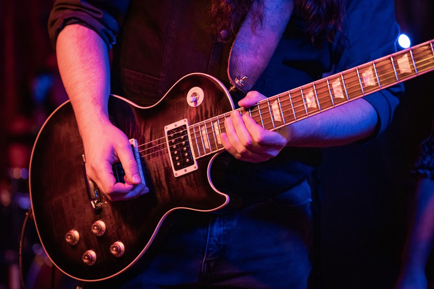 Close-up shot of hands playing an electric guitar on stage with dramatic blue lighting.