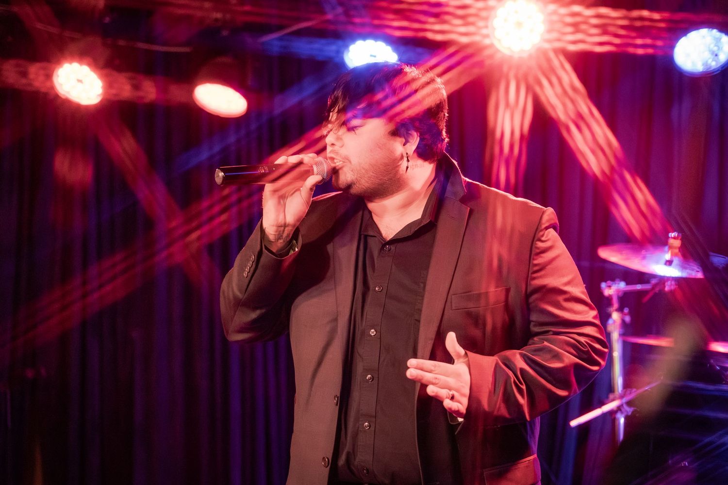 Concert performer sings on stage with dramatic purple and red lighting effects during live music performance.