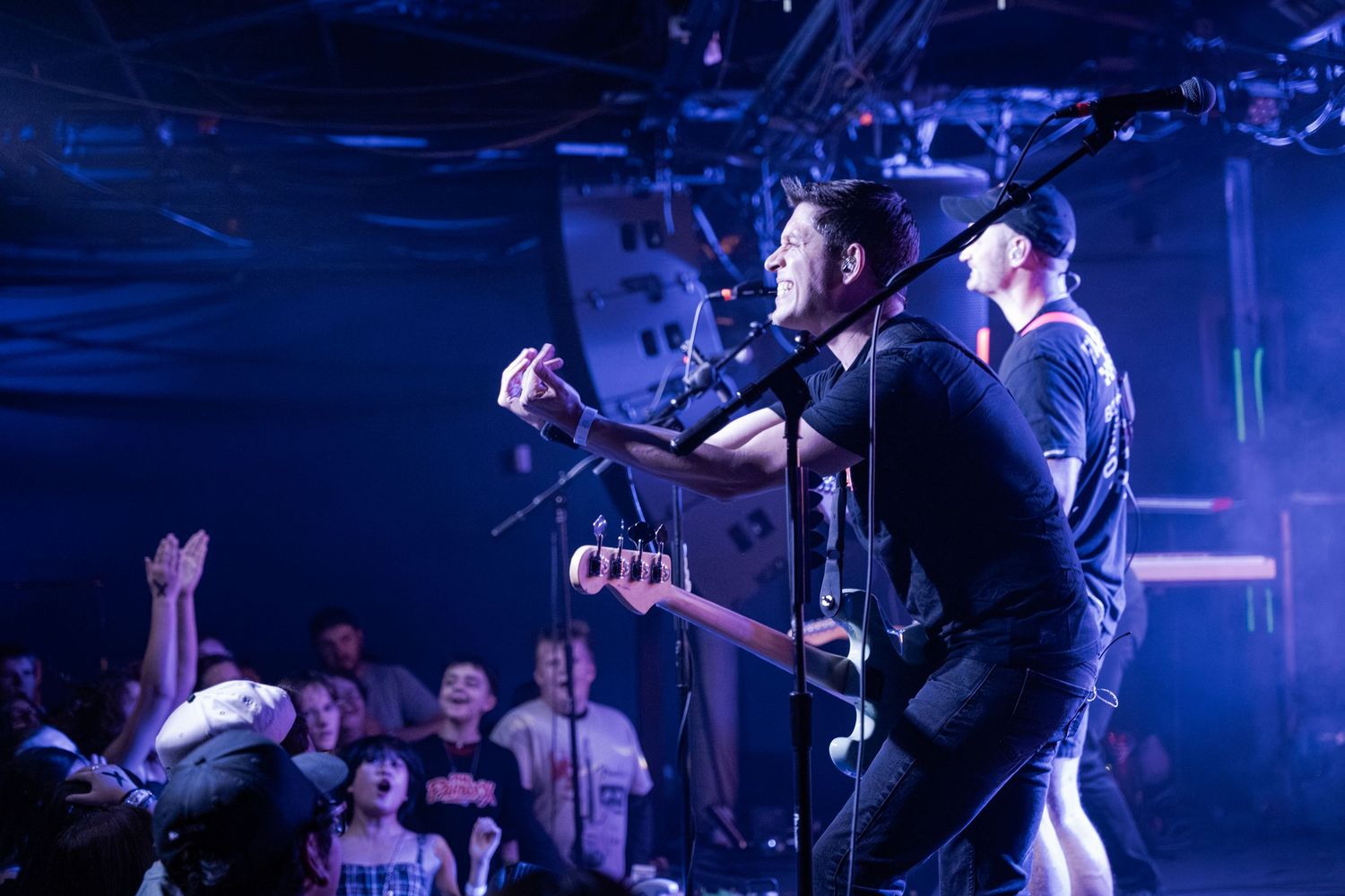 Two male musicians performing on stage with blue lighting and an energetic crowd at a live concert.