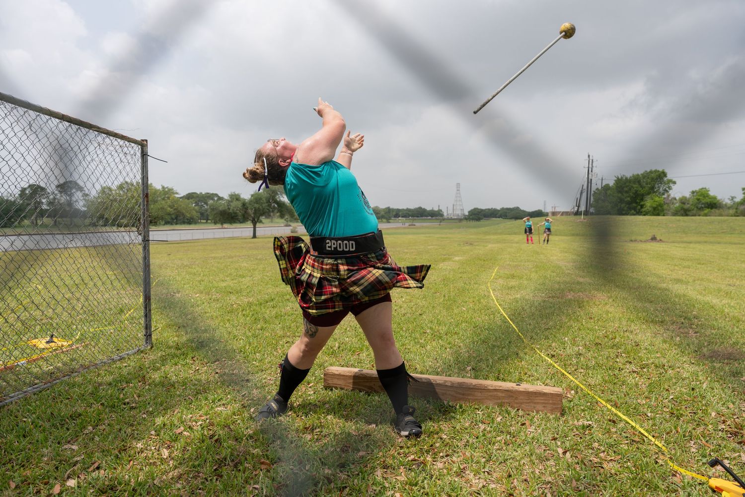 Athlete in kilt throws hammer at Highland Games competition on green field.