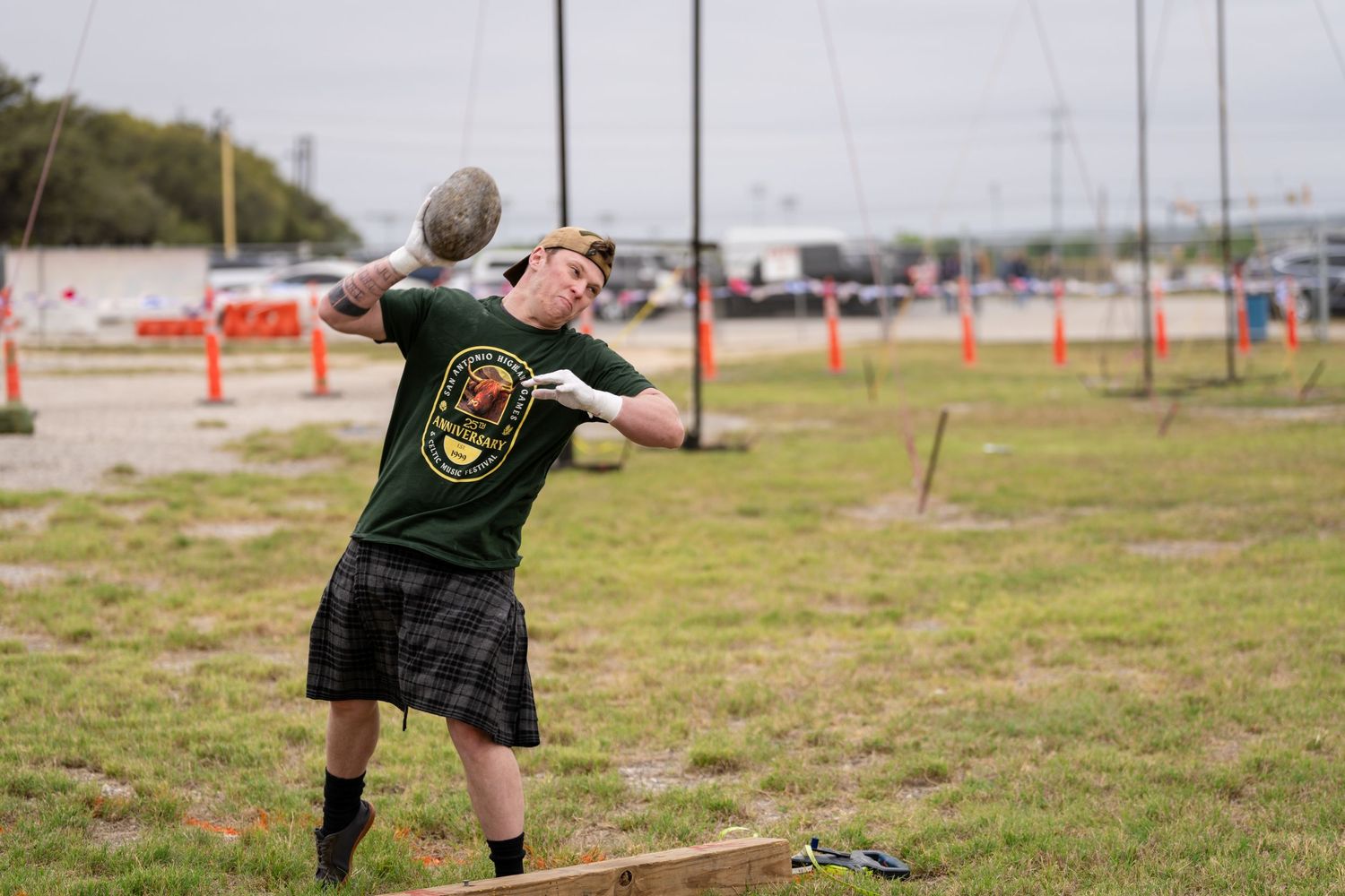 Man in kilt throwing heavy stone at Scottish Highland Games outdoor competition.
