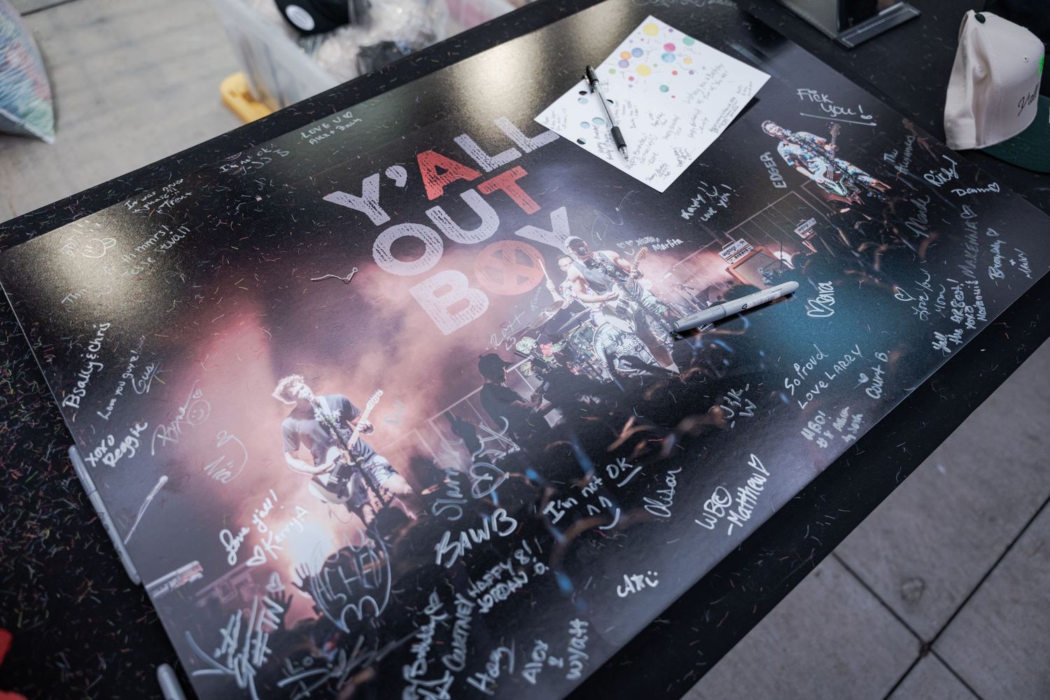 Fall Out Boy signed poster with band photo and multiple autographs displayed on a table at a fan event.