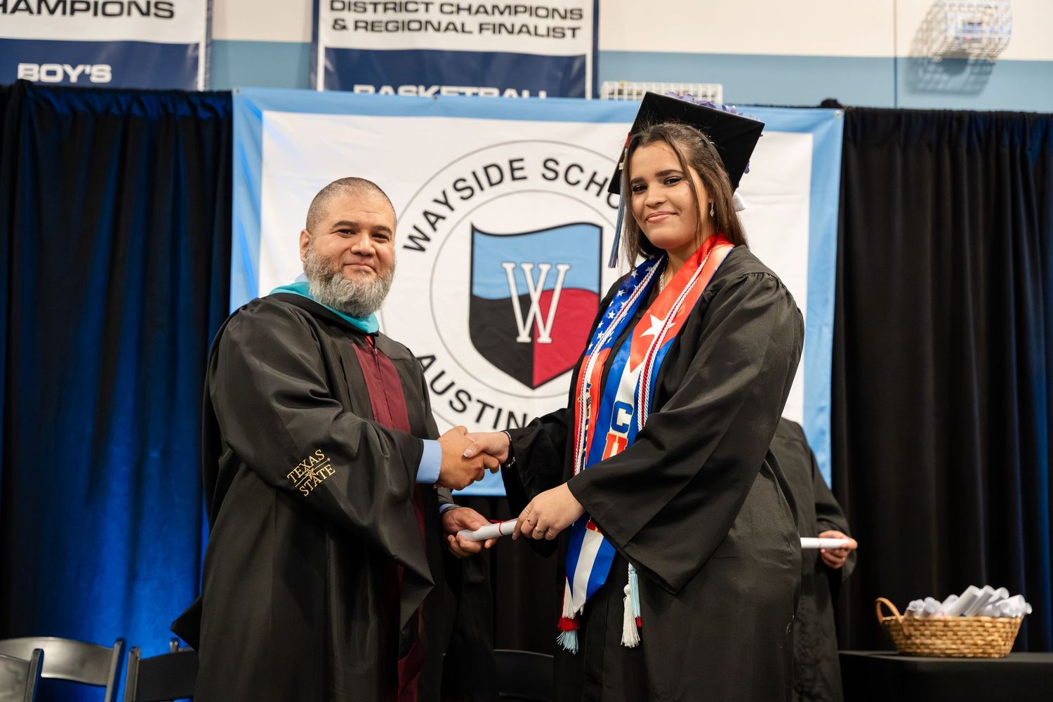 Student in graduation cap and gown shakes hands with administrator at Wayside School Austin graduation ceremony.