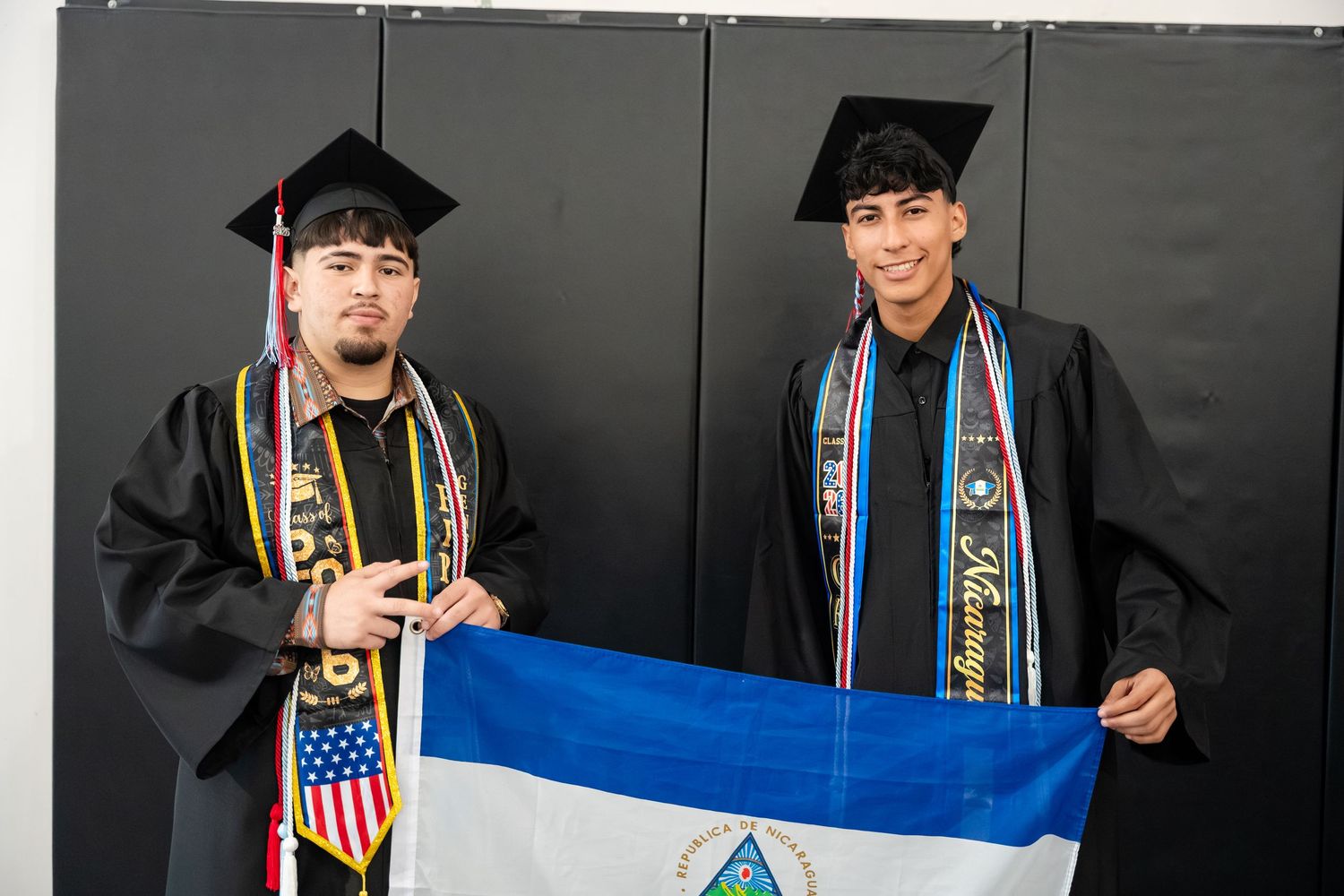 Two graduates in caps and gowns proudly hold a Nicaraguan flag during their graduation ceremony.