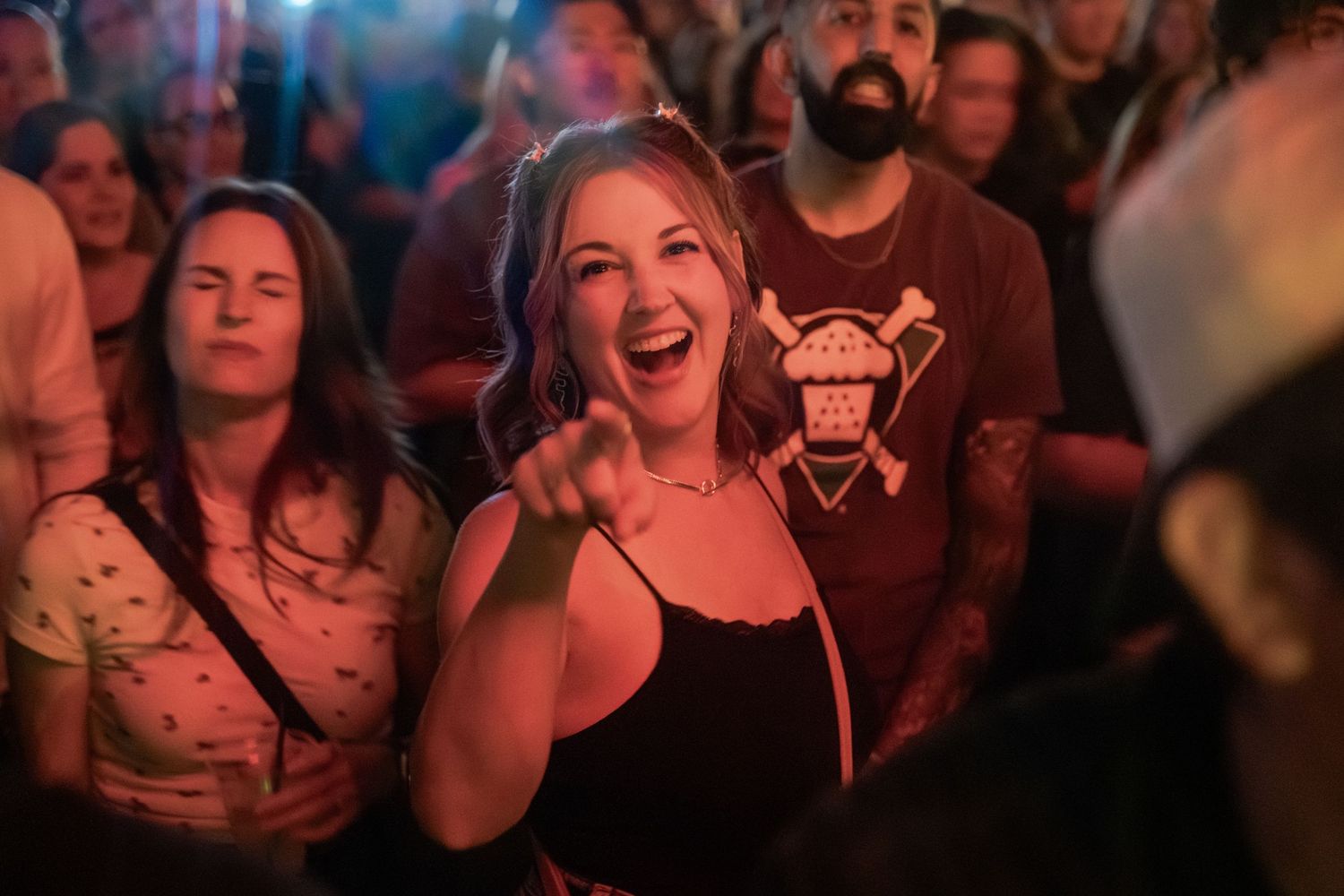 Excited woman pointing and laughing in a crowded concert venue with red ambient lighting.