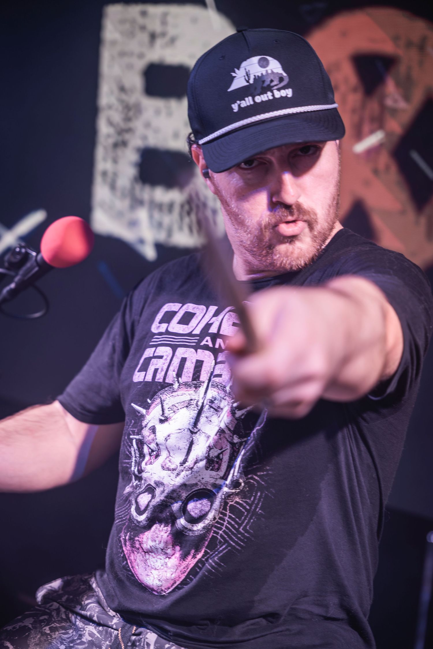 Performer wearing a black t-shirt and baseball cap in a dark concert venue setting.
