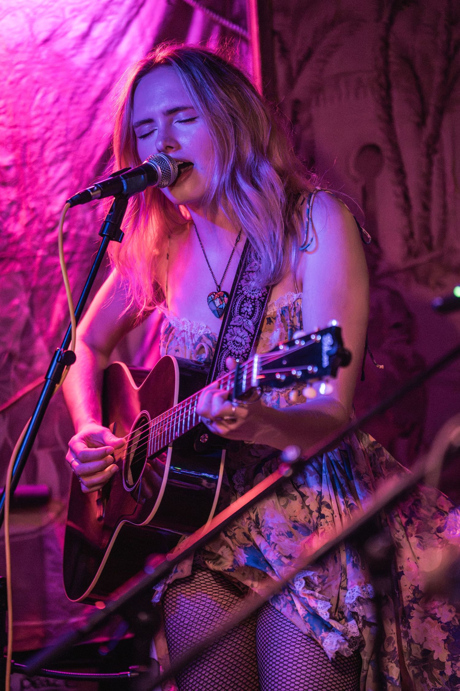 Musician performs on acoustic guitar under vibrant pink stage lighting during intimate live performance.
