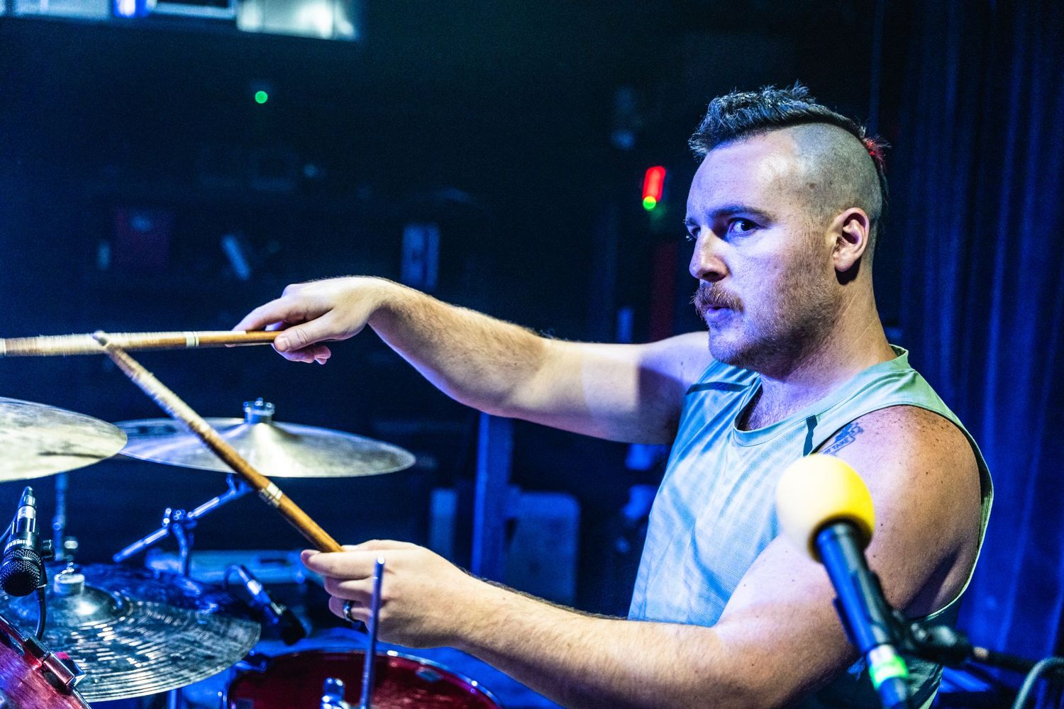 Drummer plays with intensity behind full drum kit during live performance.