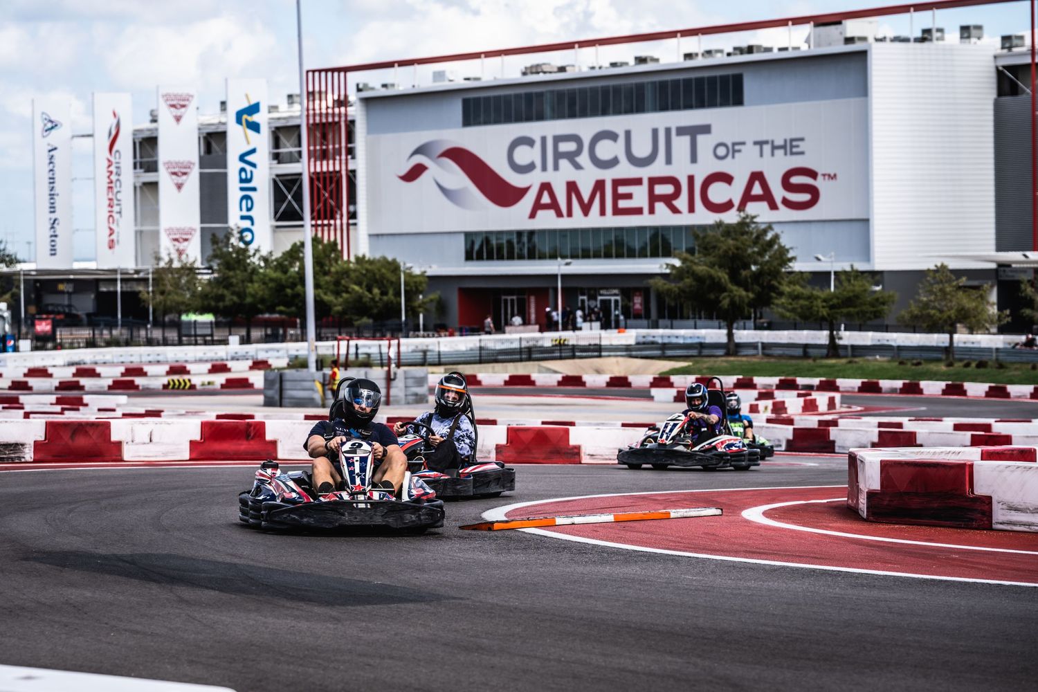 Multiple karts racing on Circuit of the Americas karting track with venue signage visible.