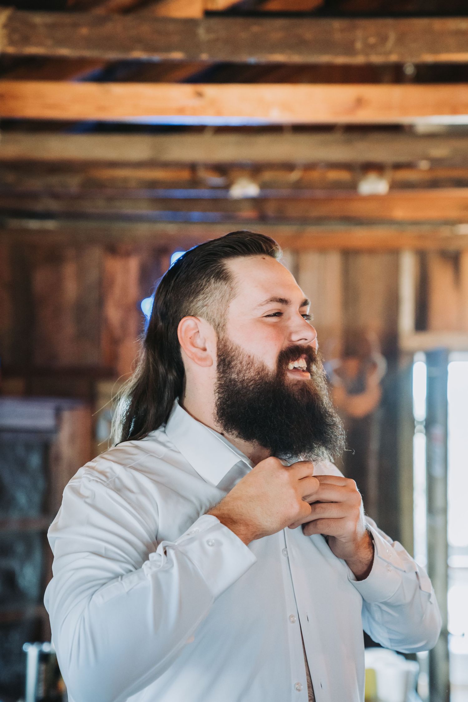 Groom adjusting his tie while getting ready in rustic wood-paneled room.