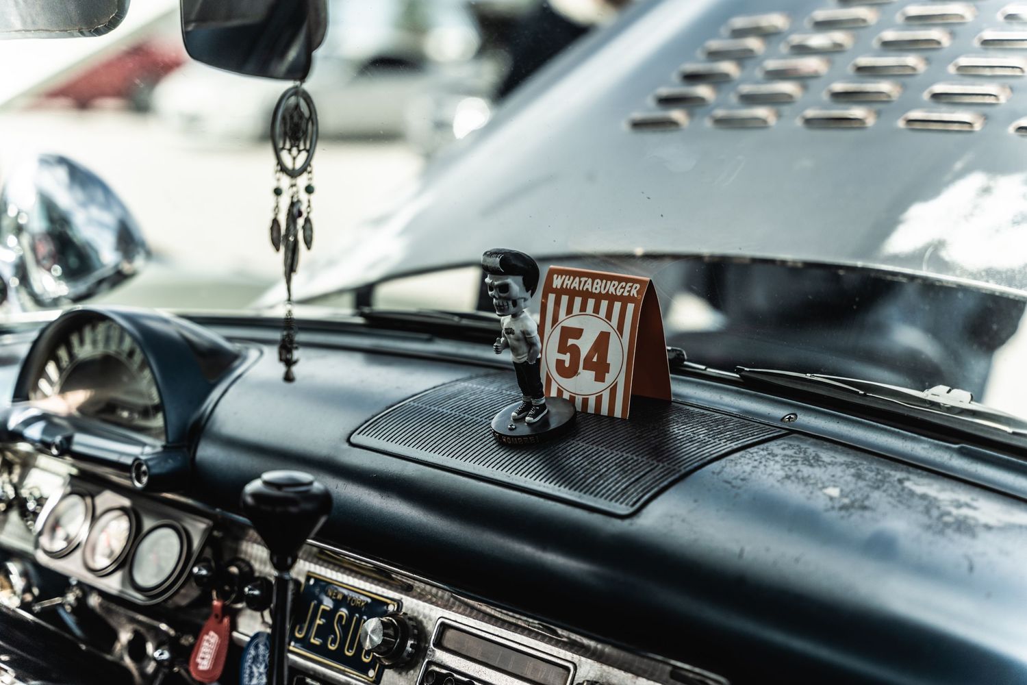 Vintage car dashboard with decorative hanging ornament and classic gauges.