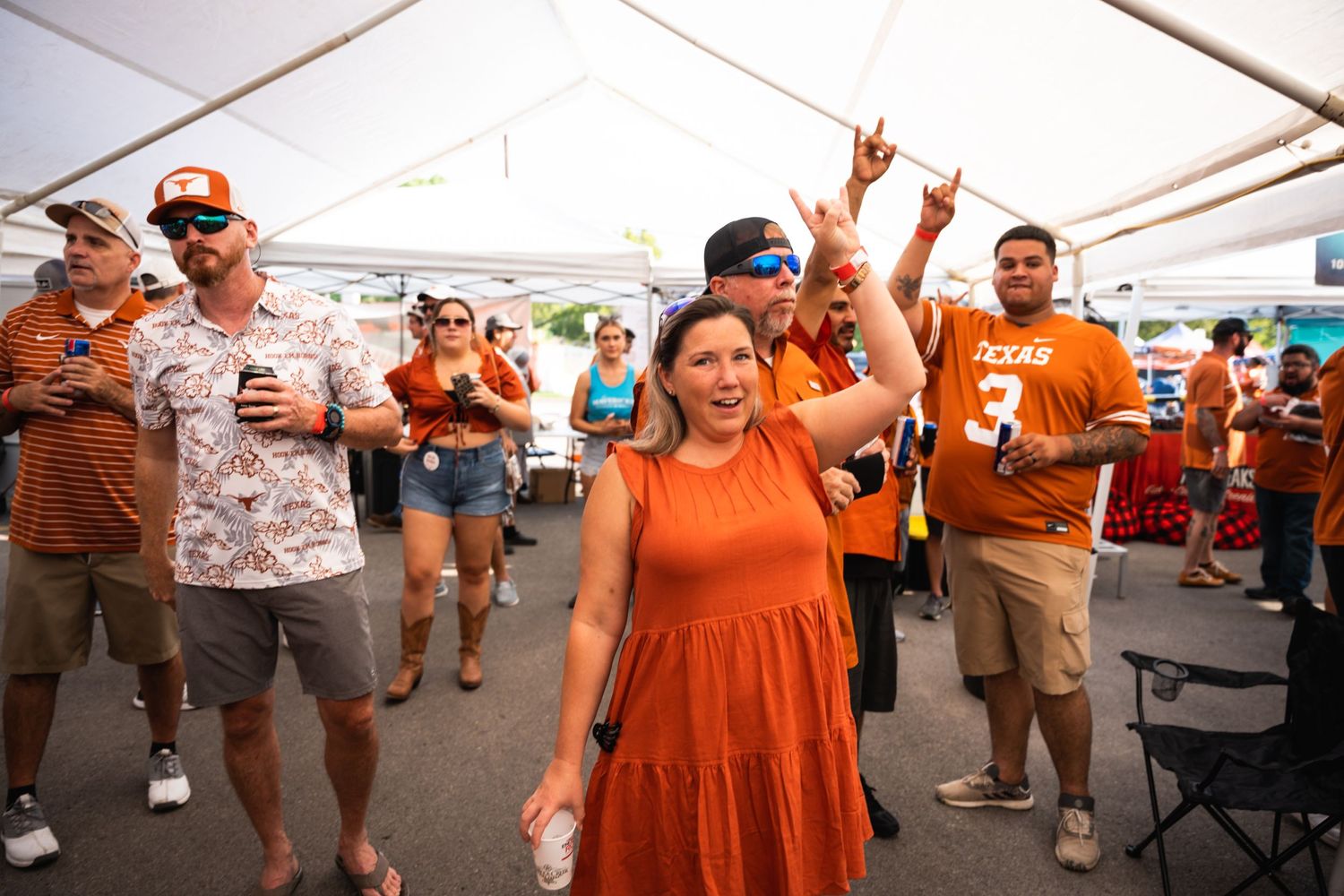 Crowd in orange attire enjoys festivities under a white tent at an outdoor gathering.