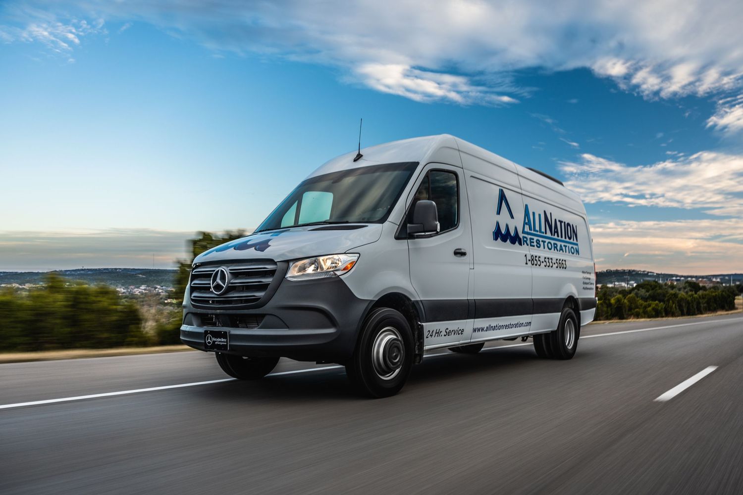 White Mercedes Sprinter delivery van driving on highway against blue sky background.