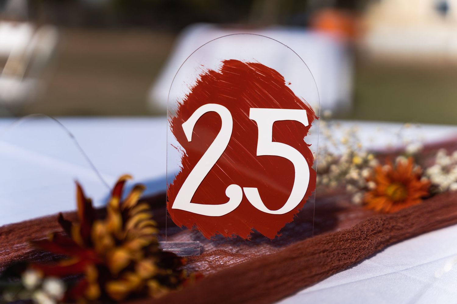 A decorative table number '25' displayed on a rustic wooden surface with fall accents.