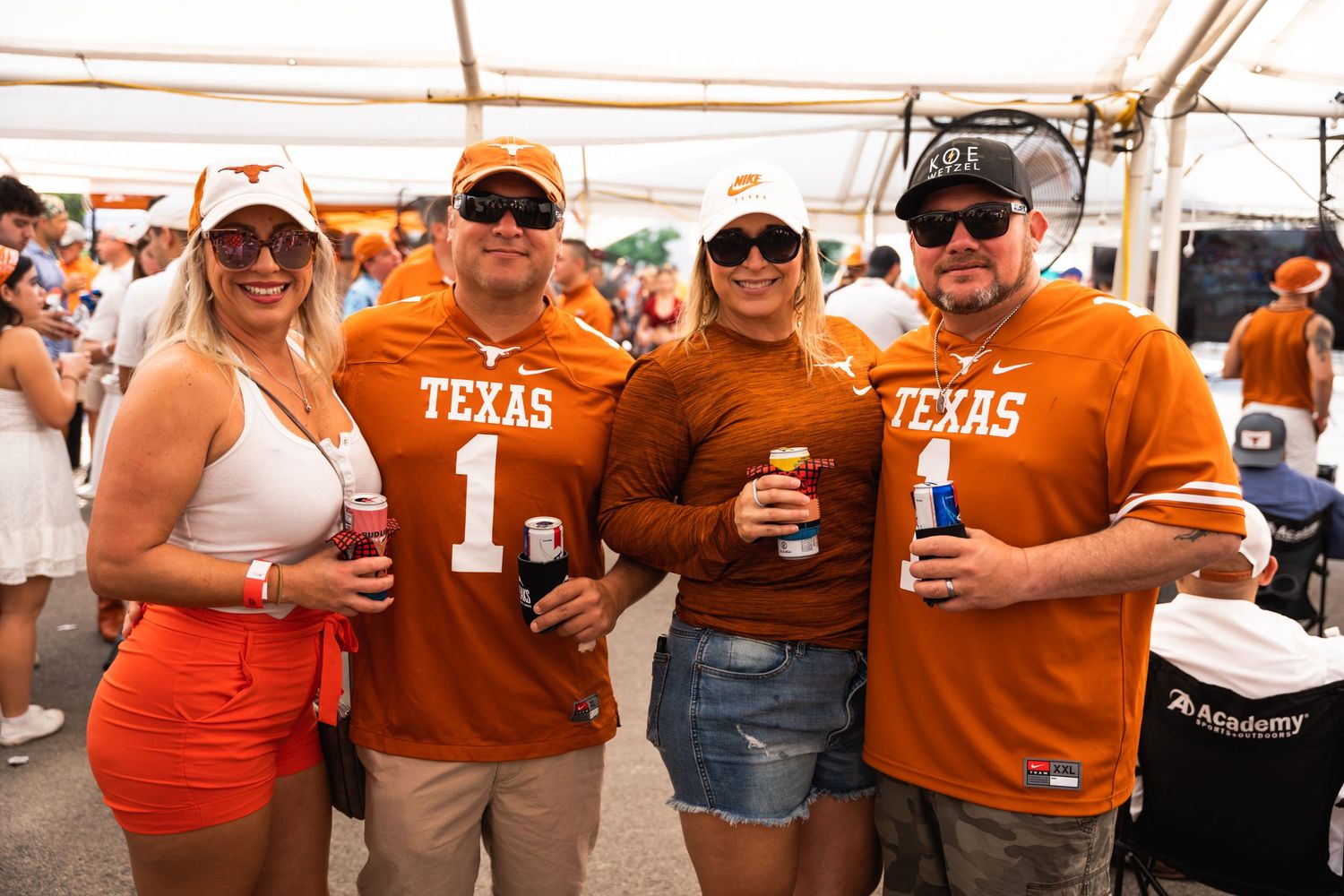 Texas fans in orange team gear pose with drinks at outdoor tailgate party.