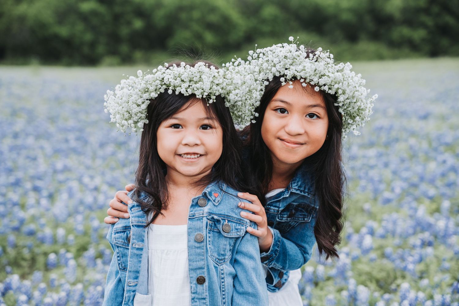 Two figures in denim jackets pose together in a field of Texas bluebonnets.